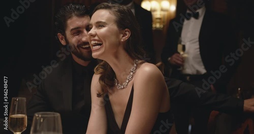 Handsome young man talking with a pretty woman sitting at dinner party. Cheerful couple at gala night.
