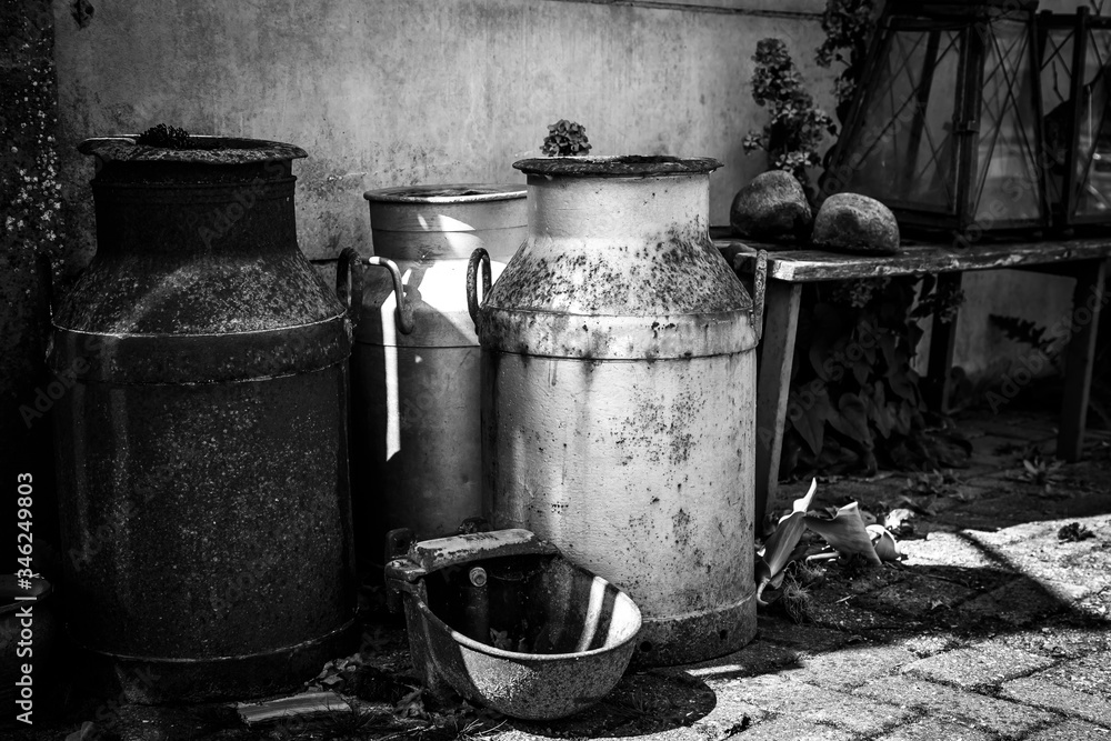 Black and white. Old rusted milk cans near the wall. Black and white. Old rusted milk cans near the wall.