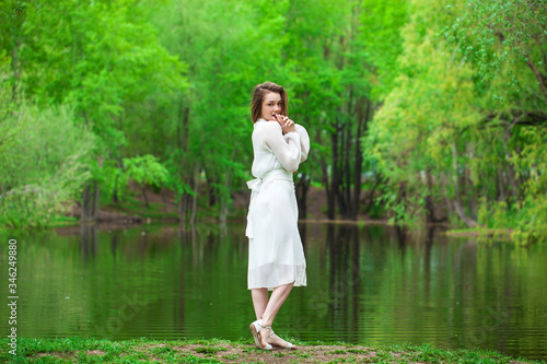 Portrait of a young beautiful woman in white dress posing by the lake