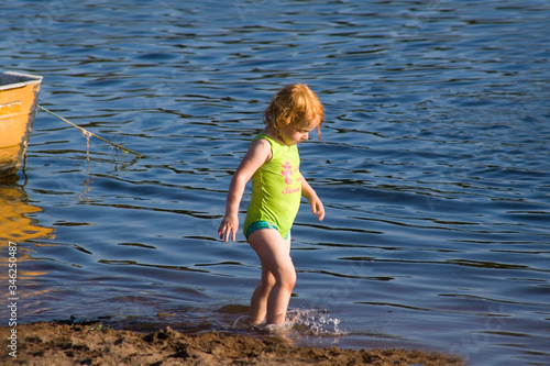 Rothaariges kleines Mädchen läuft im Badeanzug am Strand durchs Meer