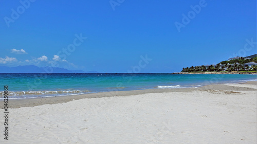 Seascape. Vietnam. Clean sand  small waves. Shades of sea water are turquoise  dark blue. Blue sky. In the distance are the silhouettes of mountains and clouds. On the coast of palm trees and villas. 