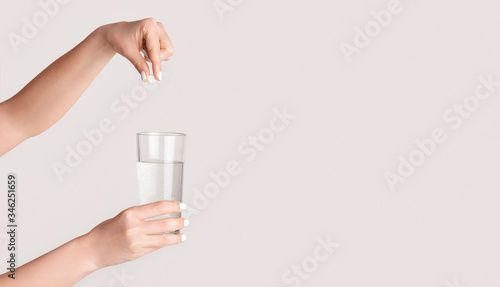 Female hands dropping pill into glass of water on light background, closeup. Blank space. Panorama
