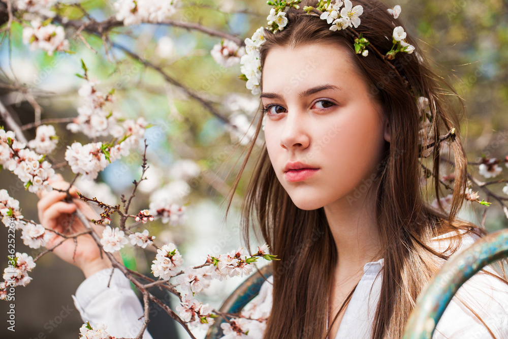 Pretty teen girl are posing in garden near blossom cherry tree with white flowers