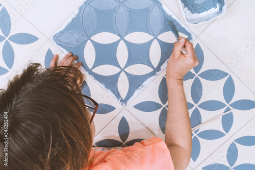 Home improvement concept: Top view of a femal painting tiles into blue using a vintage design stencil.