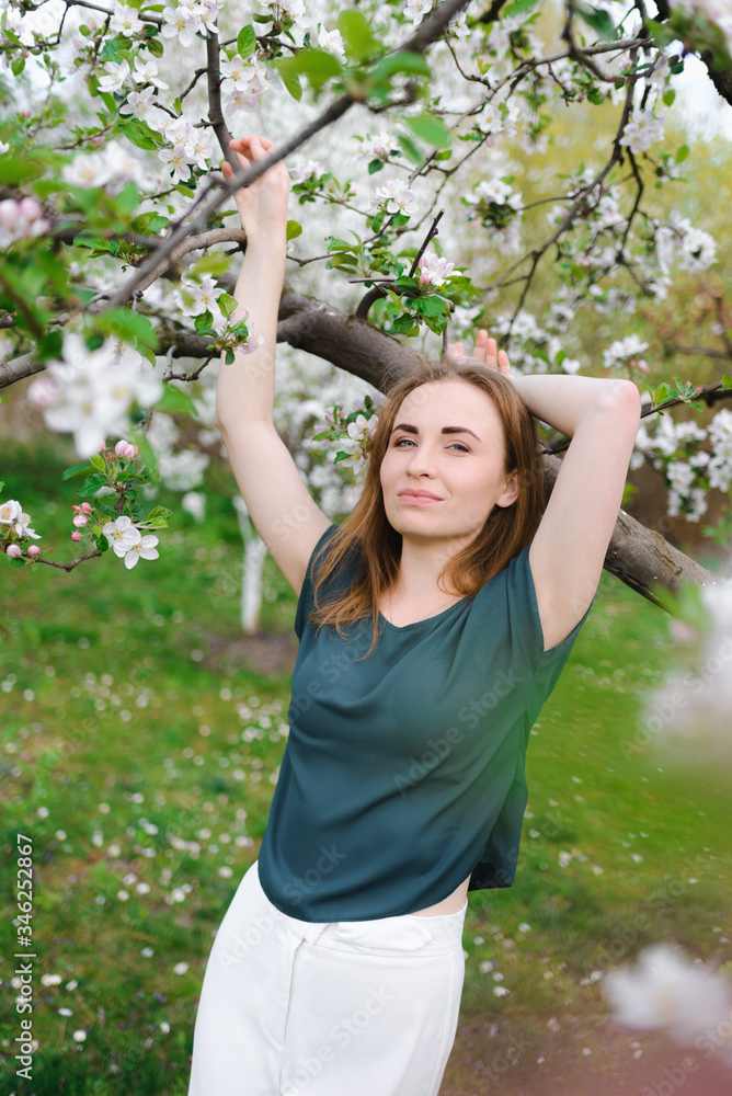 Beautiful red-haired girl posing against the background of a flowering apple tree
