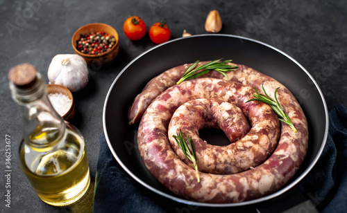 raw spiral sausage in a pan with spices and rosemary on a stone background