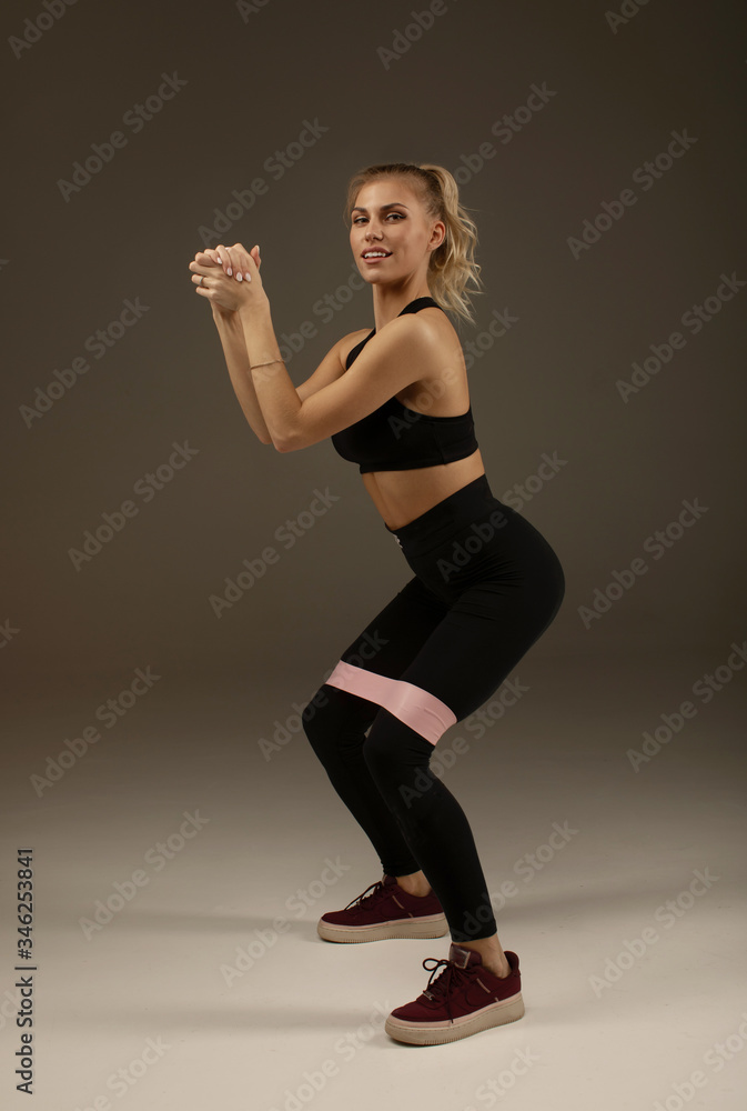 Crossfit healthy lifestyle concept. Nice charming adorable beautiful sporty fitness model lady wearing sports clothes with pink elastic band on legs. Crossfit healthy lifestyle concept. Nice charming adorable beautiful sporty fitness model lady wearing sports clothes with pink elastic band on legs.