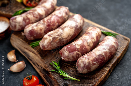 
raw sausages with spices and rosemary on
cutting board on stone background