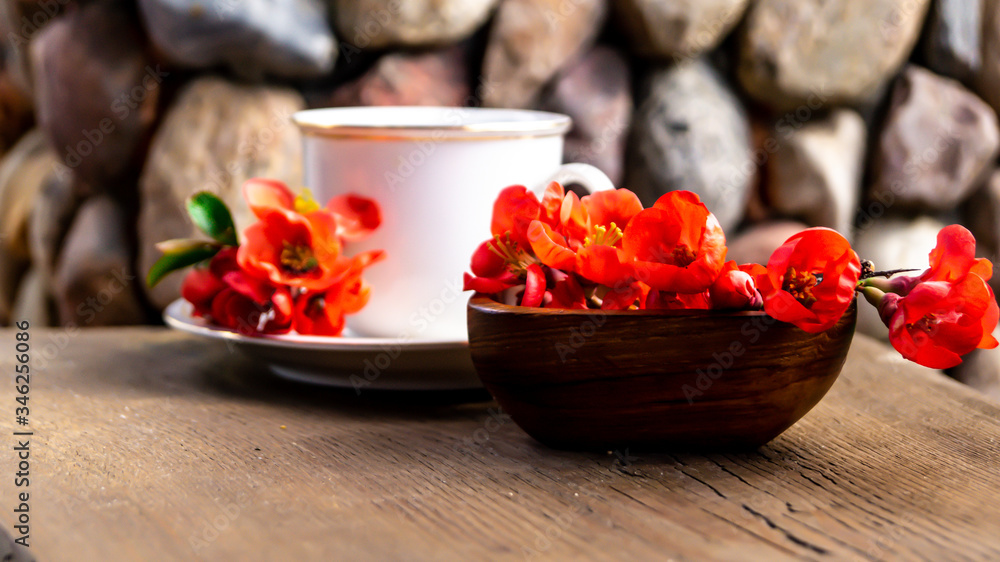 white porcelain cup with tea and red quince flowers on a wooden table in the garden