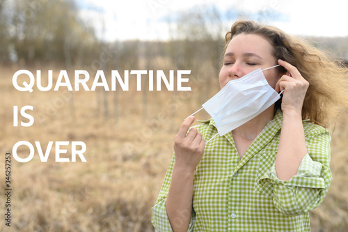 ending isolation and quarantine corona virus covid-19 concept. a young woman removes a medical mask from her face and breathing fresh air in the nature outdoor. text quarantine is over ofl font photo