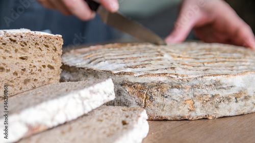 Mains coupant un Saint Nectaire sur une table en bois