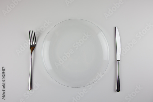Transparent plate  metal fork and knife on a white background. Table setting. For presentation of dishes and restaurants.