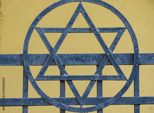 A Star of David circumscribed by a circle on a metal railings.  Behind the six pointed star is a yellow wall in the background. photo