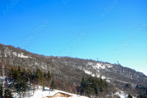 Winter cold weather in the mountains colorful landscape. Snow-covered forest in the mountains and blue sky.