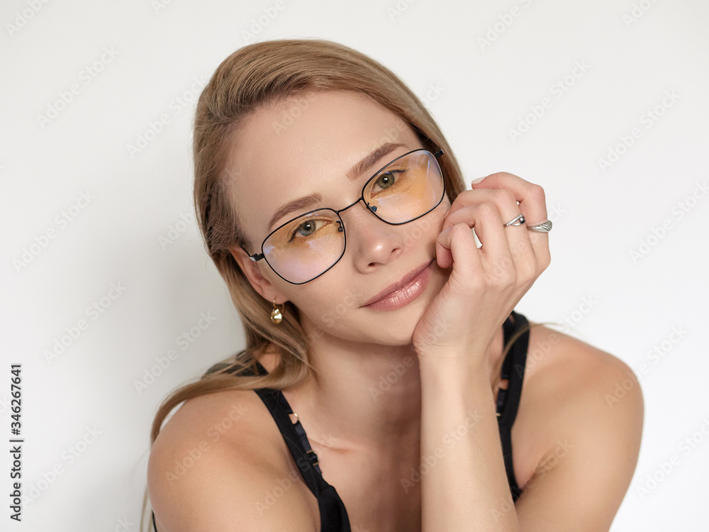 Headshot portrait of a cute natural looking blonde woman wearing simple black blouse and nerd glasses posing on a white background resting chin on hand Headshot portrait of a cute natural looking blonde woman wearing simple black blouse and nerd glasses posing on a white background resting chin on hand