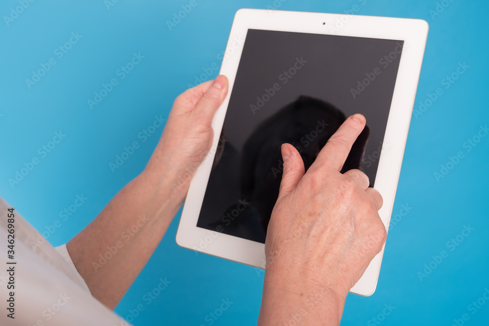 Eldery caucasian doctor lady in white coat and with tablet on blue background. Emotional portrait Eldery caucasian doctor lady in white coat and with tablet on blue background. Emotional portrait