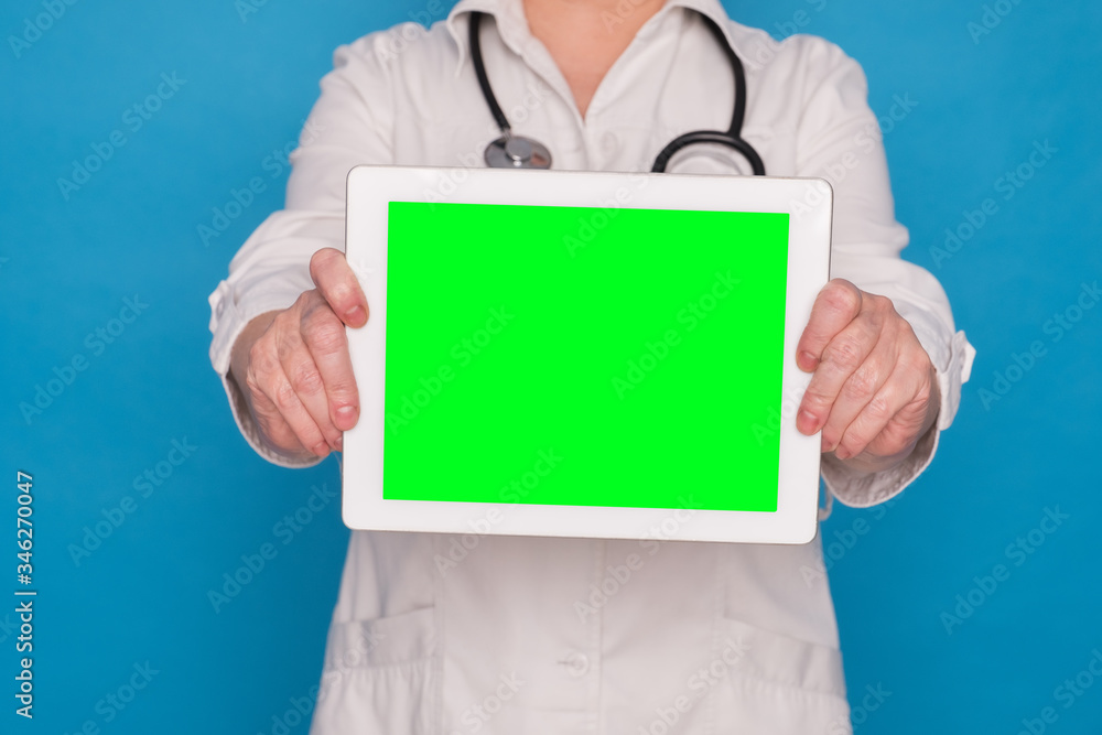Eldery caucasian doctor lady in white coat and with stethoscope and tablet on blue background. Chroma key screen on tablet Eldery caucasian doctor lady in white coat and with stethoscope and tablet on blue background. Chroma key screen on tablet