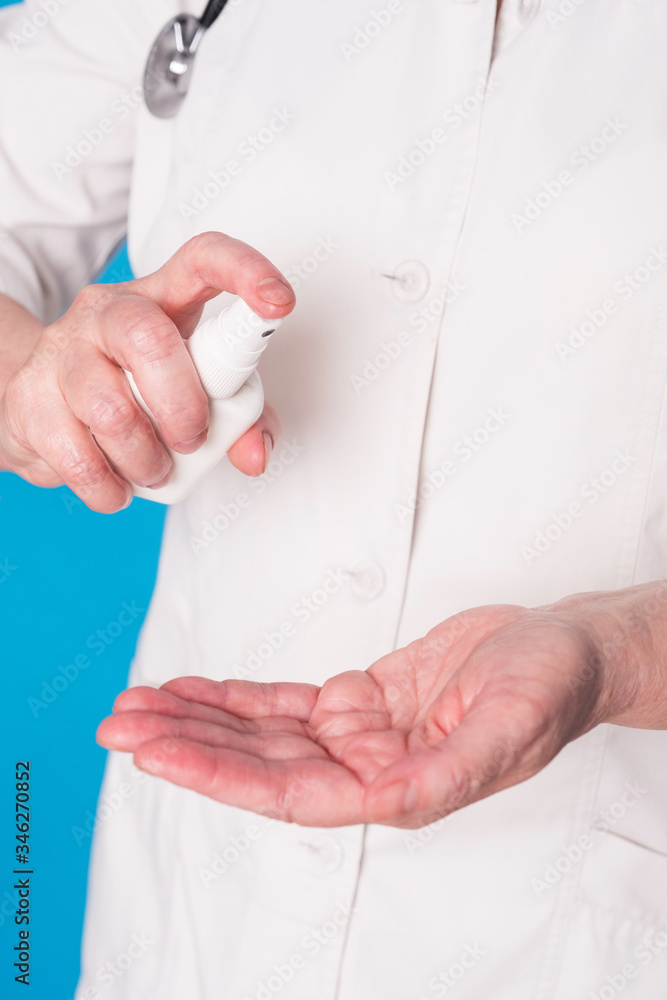 Eldery caucasian doctor lady in white coat and with stethoscope on blue background. Close up of using antiseptic Eldery caucasian doctor lady in white coat and with stethoscope on blue background. Close up of using antiseptic