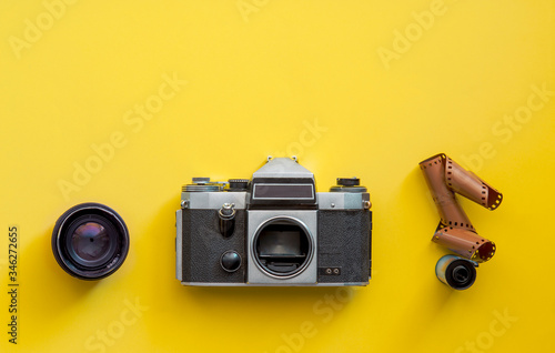 Flat lay view of retro camera, lens and film strip over pastel coloured yellow background with copy space, pop art minimal style photo