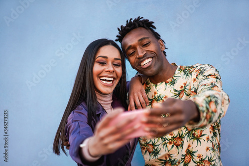 African couple doing photos and videos for social media - Young people having fun with new mobile phone trend technology - Love, fashion influencer and relationship concept - Focus on faces