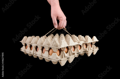 Egg tray isolated on black background. Person holding brown chicken eggs in package