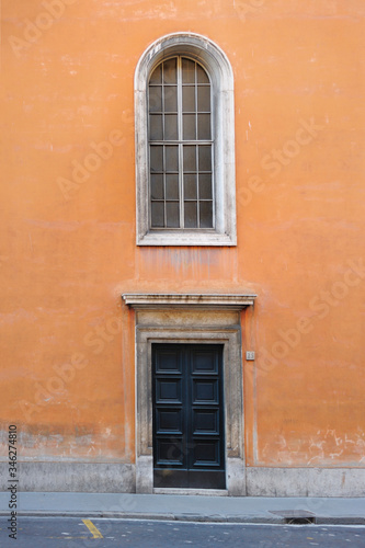 Italy, Rome - February 24, 2012: .Ancient orange building in Rome. The big black door is closed, a huge window is located above it. The street is empty. © Nosenko Olga