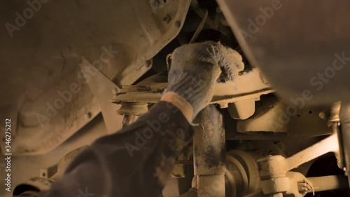 Hands in gloves and work clothes are repairing a spare part of a car in a garage, closeup.