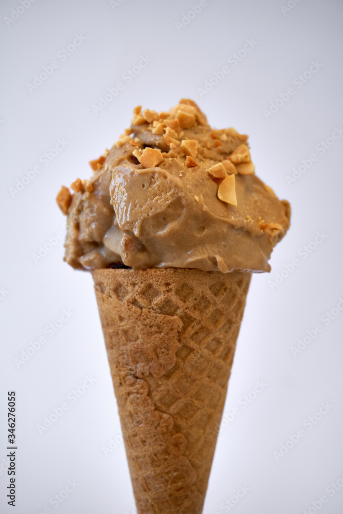 Peanut butter banana ice cream cone with sprinkles of peanuts on top on a white background