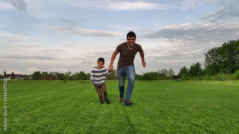 father and son run through a green field in slow motion father and son run through a green field in slow motion