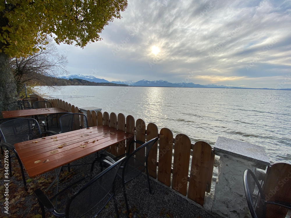 View of the Chiemsee lake in Bavaria, Germany. Mountains at the horizon and tables, chairs in the foreground. View of the Chiemsee lake in Bavaria, Germany. Mountains at the horizon and tables, chairs in the foreground.