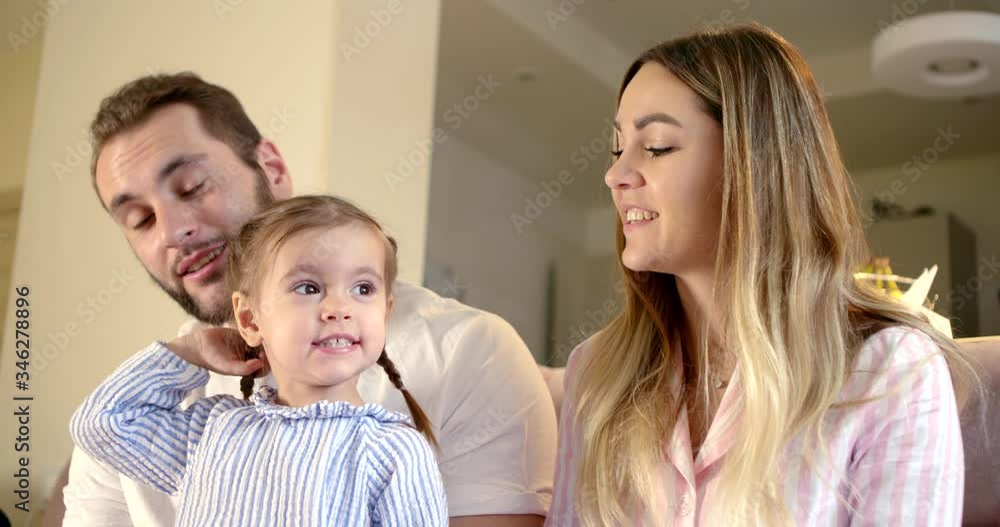 A close-up portrait of a young family sitting at home in self-isolation on a sofa and communicating with someone via video link from a mobile phone.