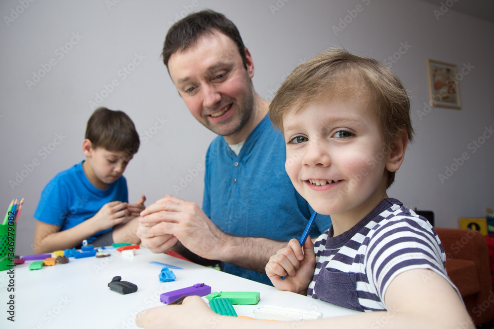 Obraz premium Dad with children to sculpt from plasticine at home. Time spent with your family. An idea for working with children during a period of self-isolation.