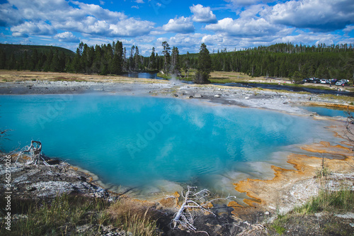 Basin with blue shade of thermal microorganisms inside with orange brown color by sides in Yellowstone National park United States, Travel background with geysers and hot springs, famous landmarks.
