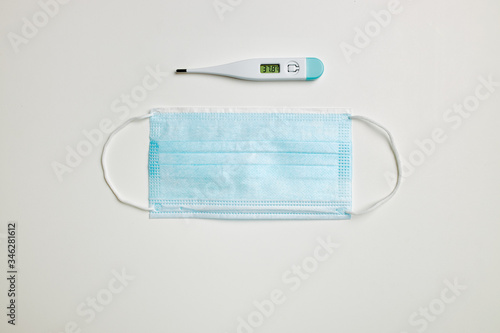 Blue face mask and digital thermometer on white background.