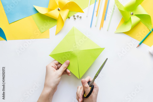 How to make paper green windmill toy with children at home. Step by step instructions. Hands making DIY summer project. Step 5. Cut sheet in lines to circle in center, getting half-cut triangles.