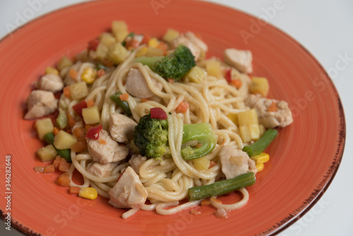 Spaghetti with chicken and vegetables is laid out on a bright orange platter. Close up. Mouth-watering food.