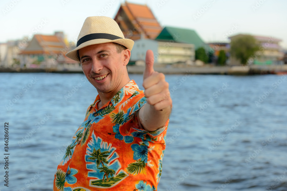 Happy young handsome tourist man at pier against view of the river