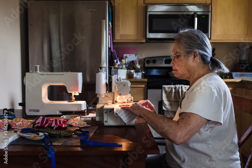 Side view of senior woman sewing masks from fabric at home