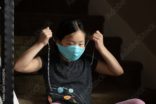 Asian girl pulls strings of cloth face mask around head photo