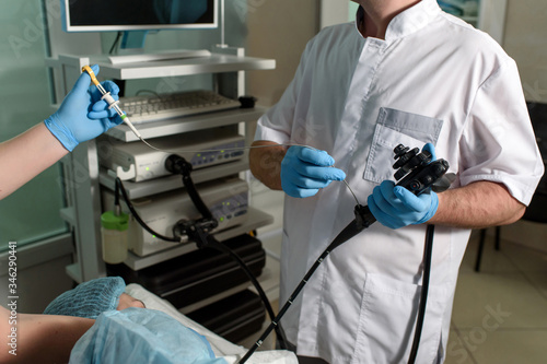 Endoscopic examination in a modern clinic. The doctor holds an endoscope in his hand, the nurse holds the forceps for a biopsy of the patient. Medical manipulations and examination.