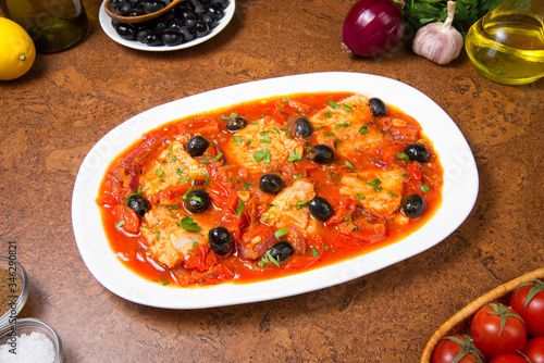 Pan seared fish with tomatoes and olives on an brown table. Selected focus.