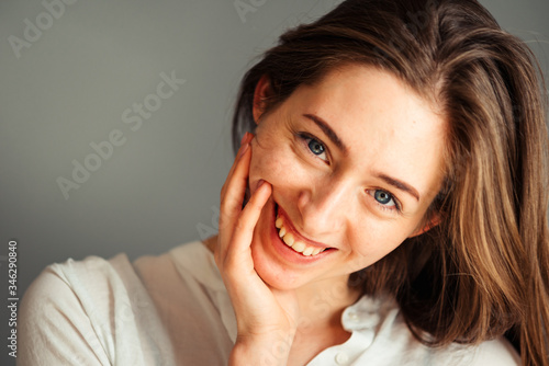 Close-up portrait of a smiling young girl in a white shirt on a gray background. in a good mood. Without retouching and makeup.