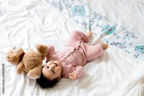 portrait of a toddler girl smiling, lying on a bed with a teddy bear. space for text