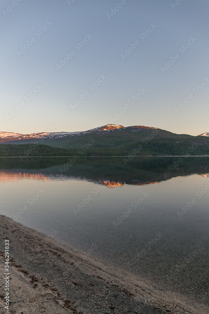 Norwegian fjord and mountains surrounded by clouds, midnight sun, polar day, ideal fjord reflection in clear water. selective focus. Photo taken at midnight sun