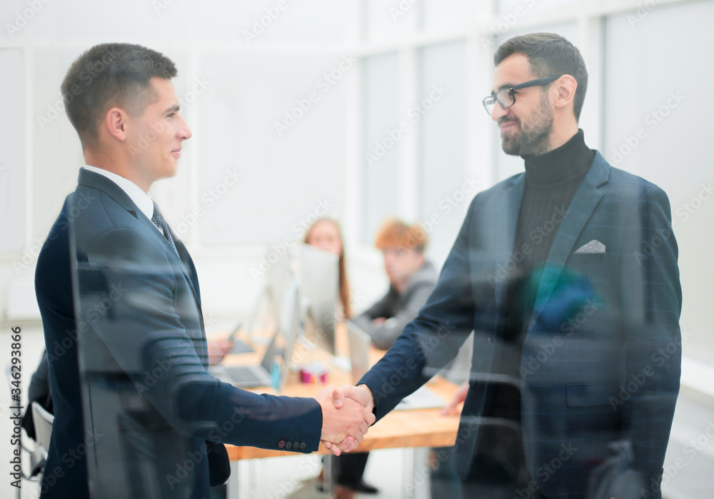 through the glass. business partners handshake in the office through the glass. business partners handshake in the office