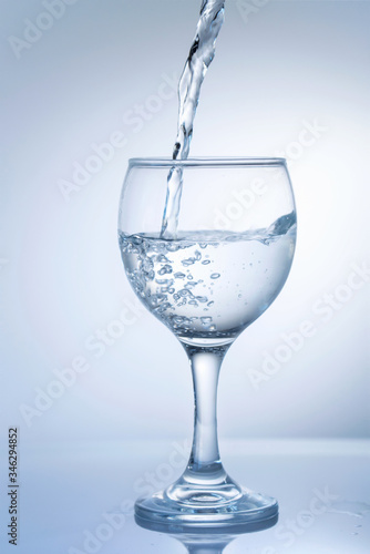 Water pouring into wine glass on a white background, close up