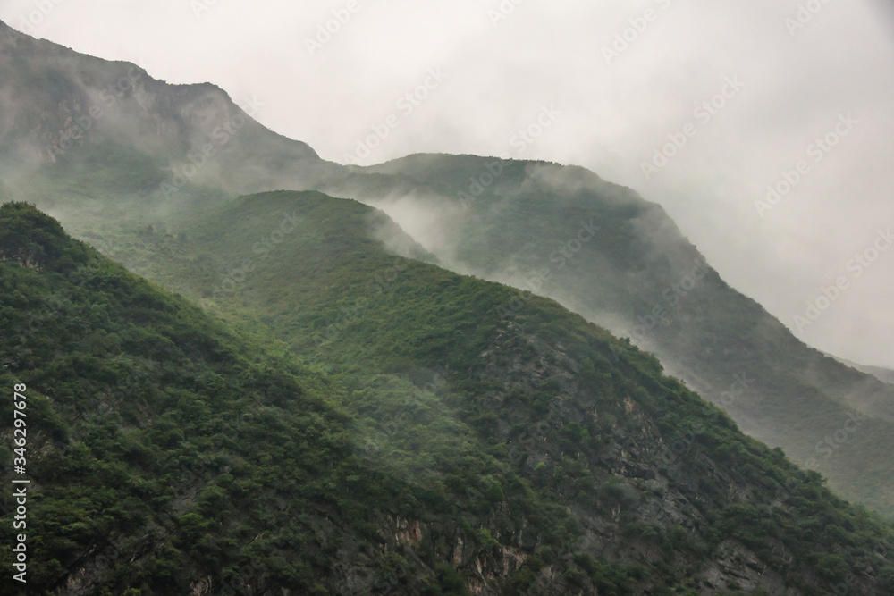 Baidicheng, China - May 7, 2010: Qutang Gorge on Yangtze River. Landscape of gray cloudscape descends in waves along slopes of green covered mountain.