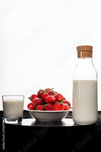 A bottle of milk, a plate of strawberries, a glass of milk on a black cloth on a white background