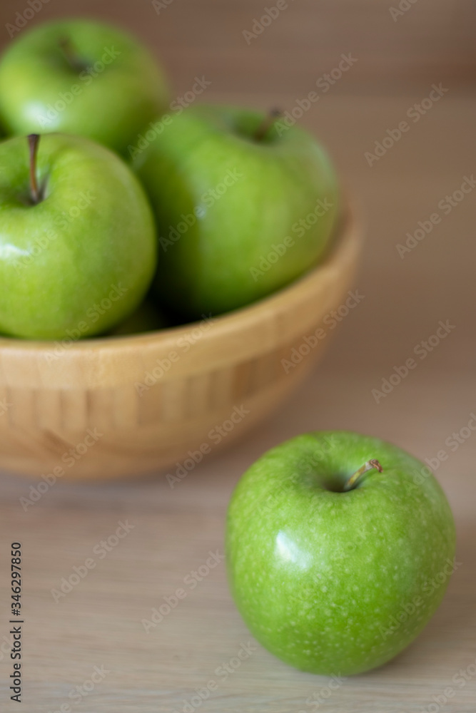 Green apples in a wooden bowl and one green Apple lying next to the bowl on the table. Green apples in a wooden bowl and one green Apple lying next to the bowl on the table.