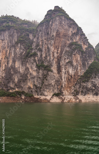 Baidicheng  China - May 7  2010  Qutang Gorge on Yangtze River. Straigth down brown cliff with some green foliage on top and darker patches above green water.